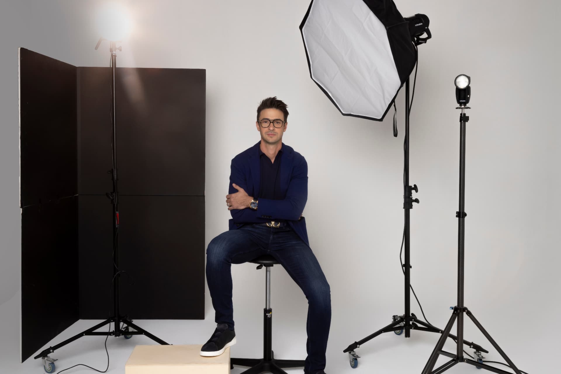 Anthony Kennada seated on a stool in a photography studio, framed by softboxes and light stands